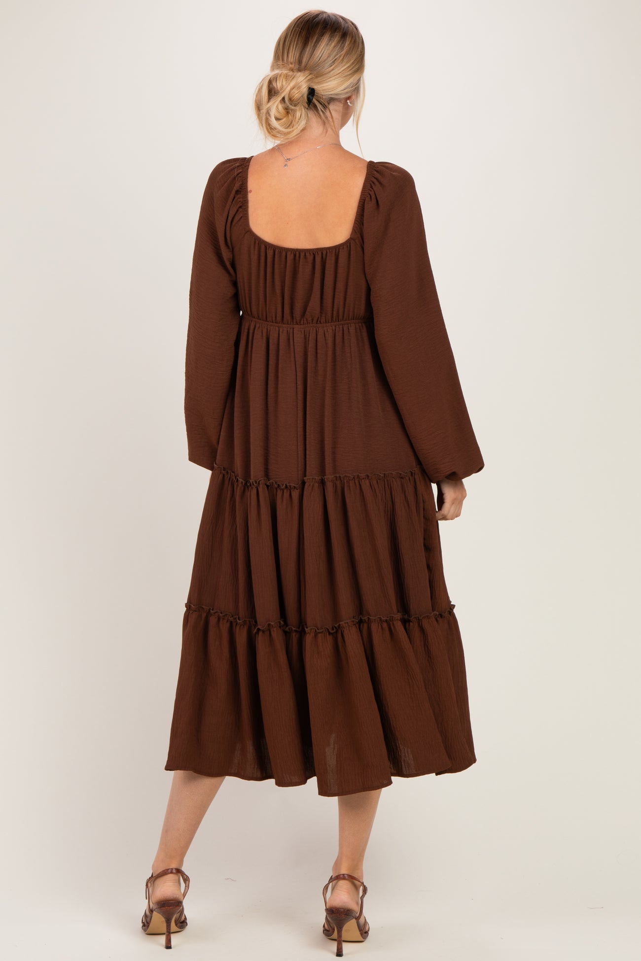woman wearing a brown tiered midi dress with long sleeves and a square back revealing the shoulder and upper back