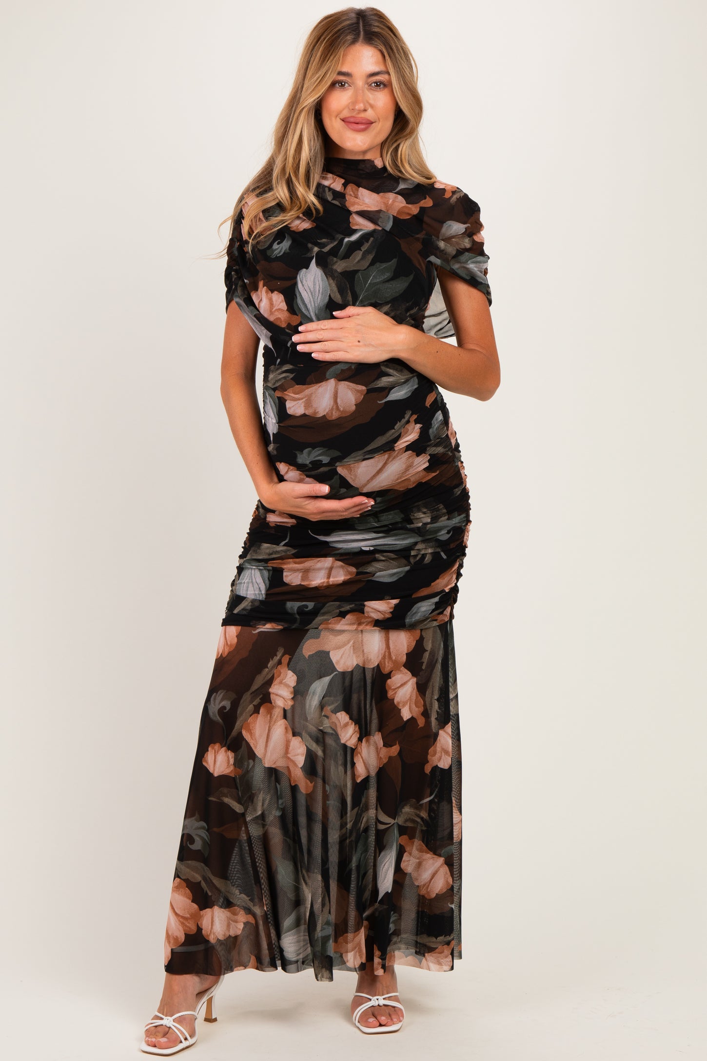 woman wearing a black floral print maternity dress with ruching and a flowing skirt, cradling her baby bump