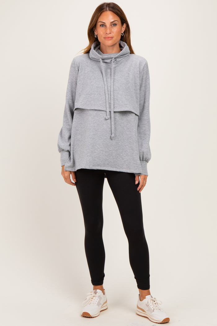 woman wearing a gray cowl neck oversized sweatshirt layered over a long sleeve top with black leggings and sneakers