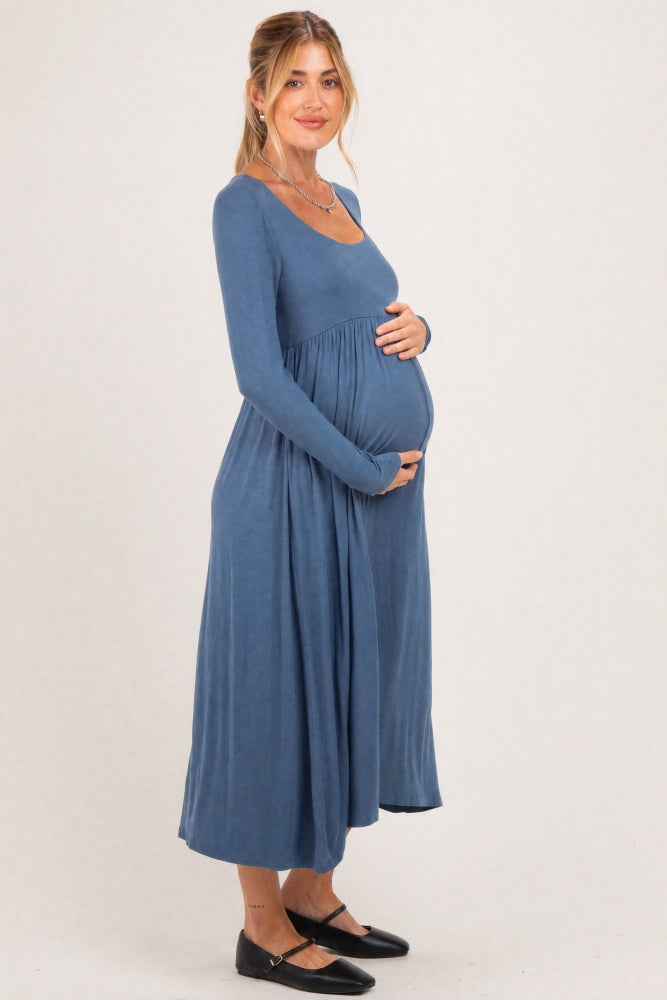 woman wearing a dusty blue long sleeve maternity dress and cradling her baby bump