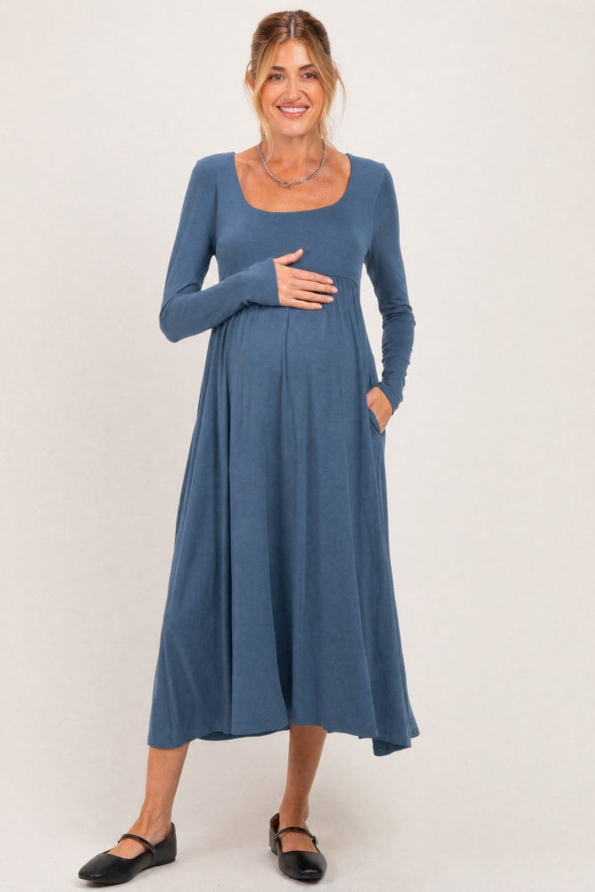 woman wearing a blue long sleeve maternity dress with a scoop neckline and pockets, cradling her baby bump