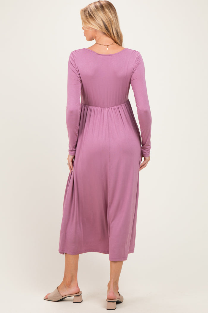 woman wearing a mauve long sleeve maternity dress with a fitted waist and flowing skirt