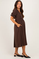 woman wearing a brown maternity dress with puff sleeves and pockets, showing her baby bump