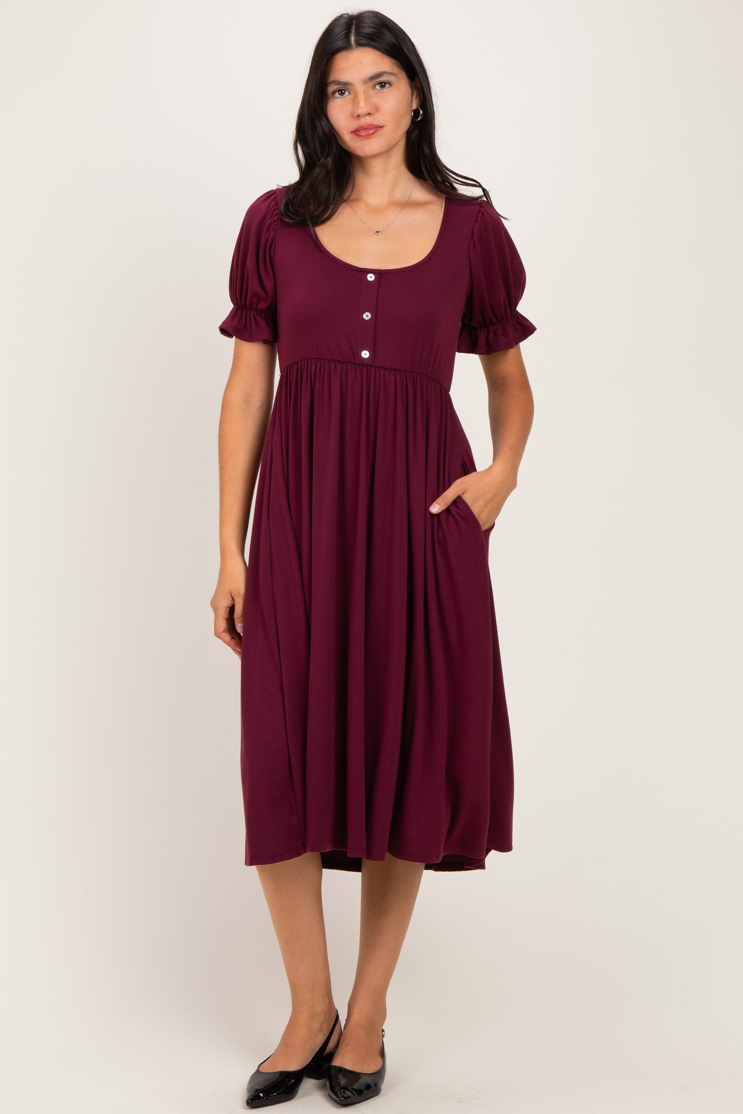 woman wearing a burgundy midi dress with short puff sleeves and decorative buttons, featuring a fitted bodice and pocket