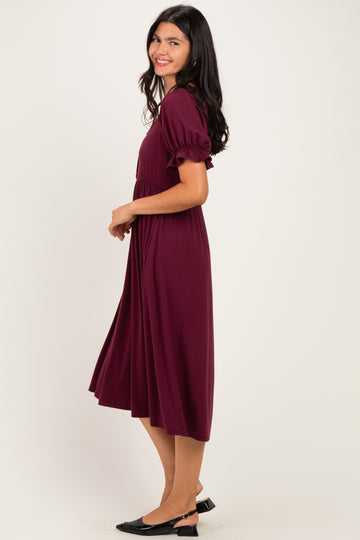woman wearing a wine red midi dress with puff sleeves, smiling and standing sideways