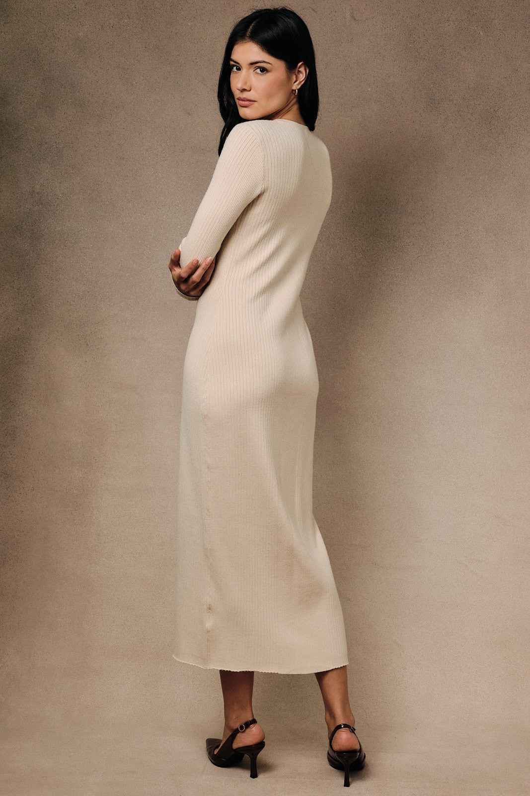 woman wearing a cream long sleeve ribbed midi dress, standing with her back to the camera