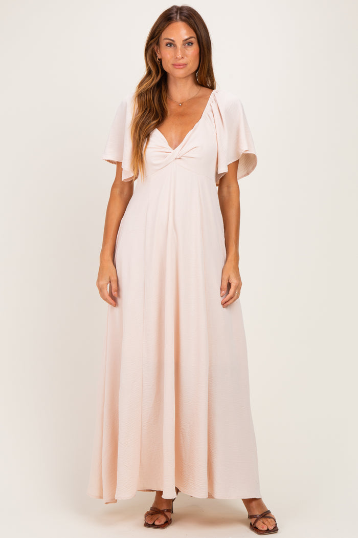 woman wearing a light pink maxi dress with flutter sleeves and a knotted front detail