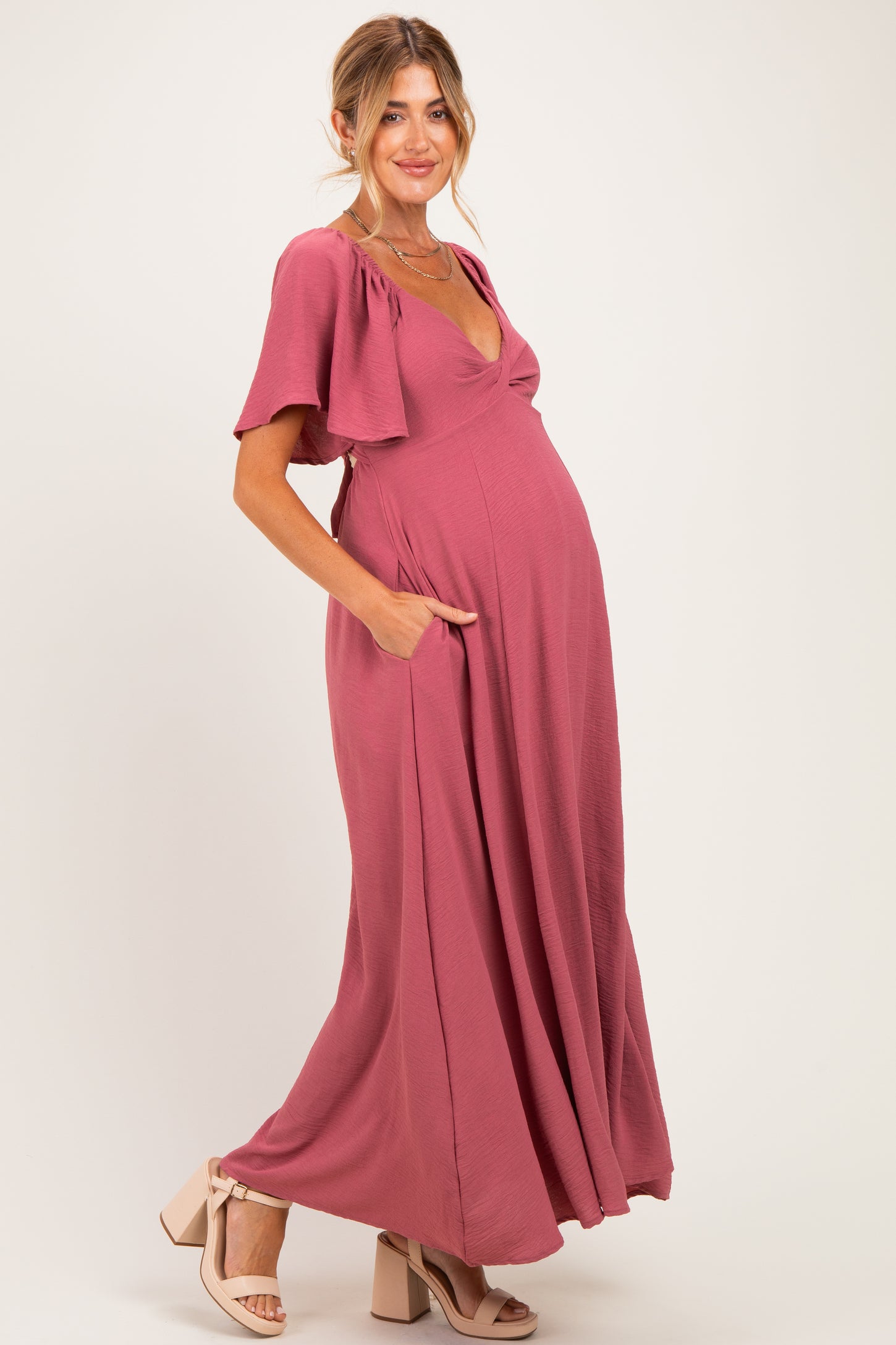woman wearing a dusty rose maternity maxi dress with flutter sleeves and pockets, showing her baby bump