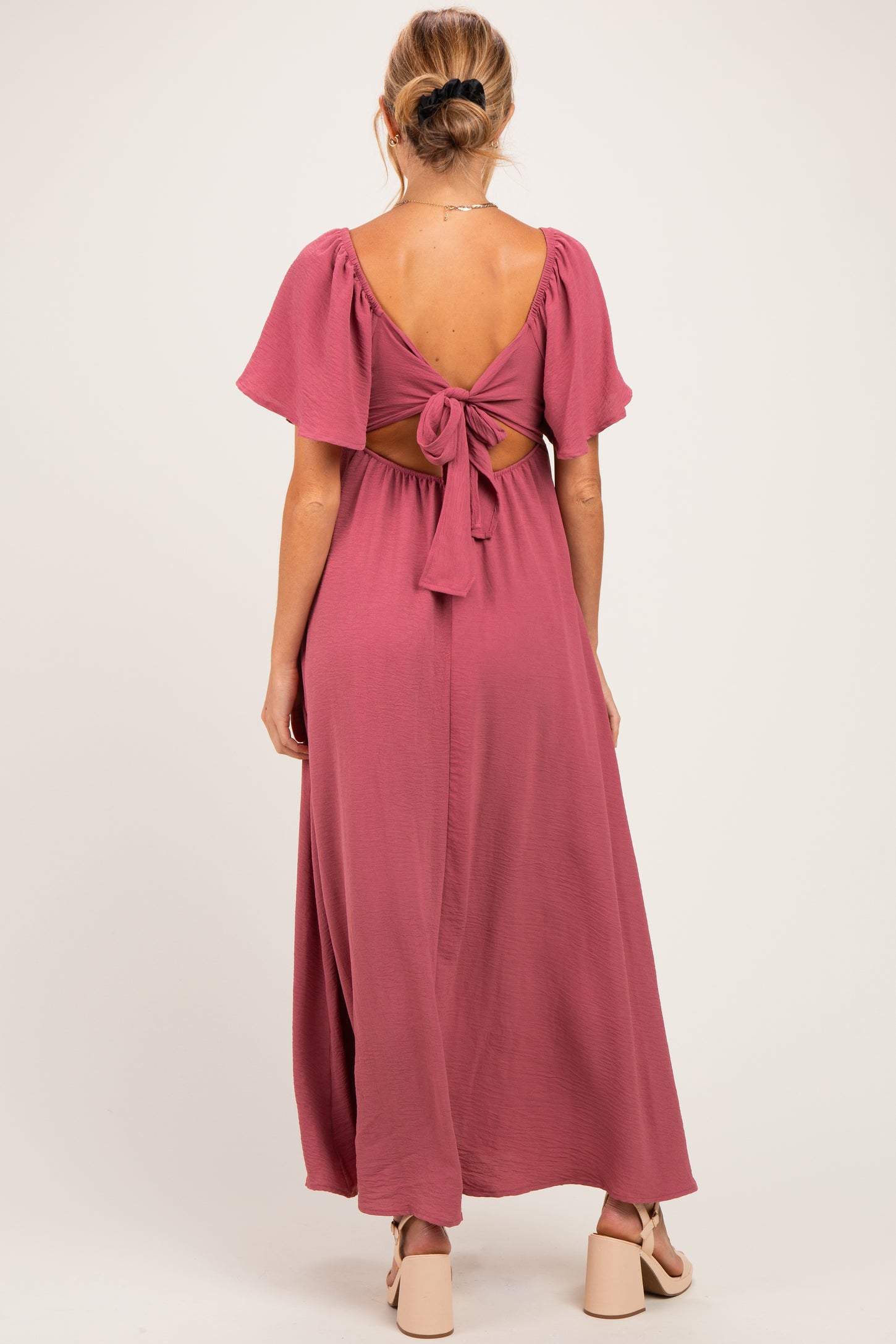 woman wearing a dusty rose maternity dress with flutter sleeves and a tied back detail, showcasing a baby bump
