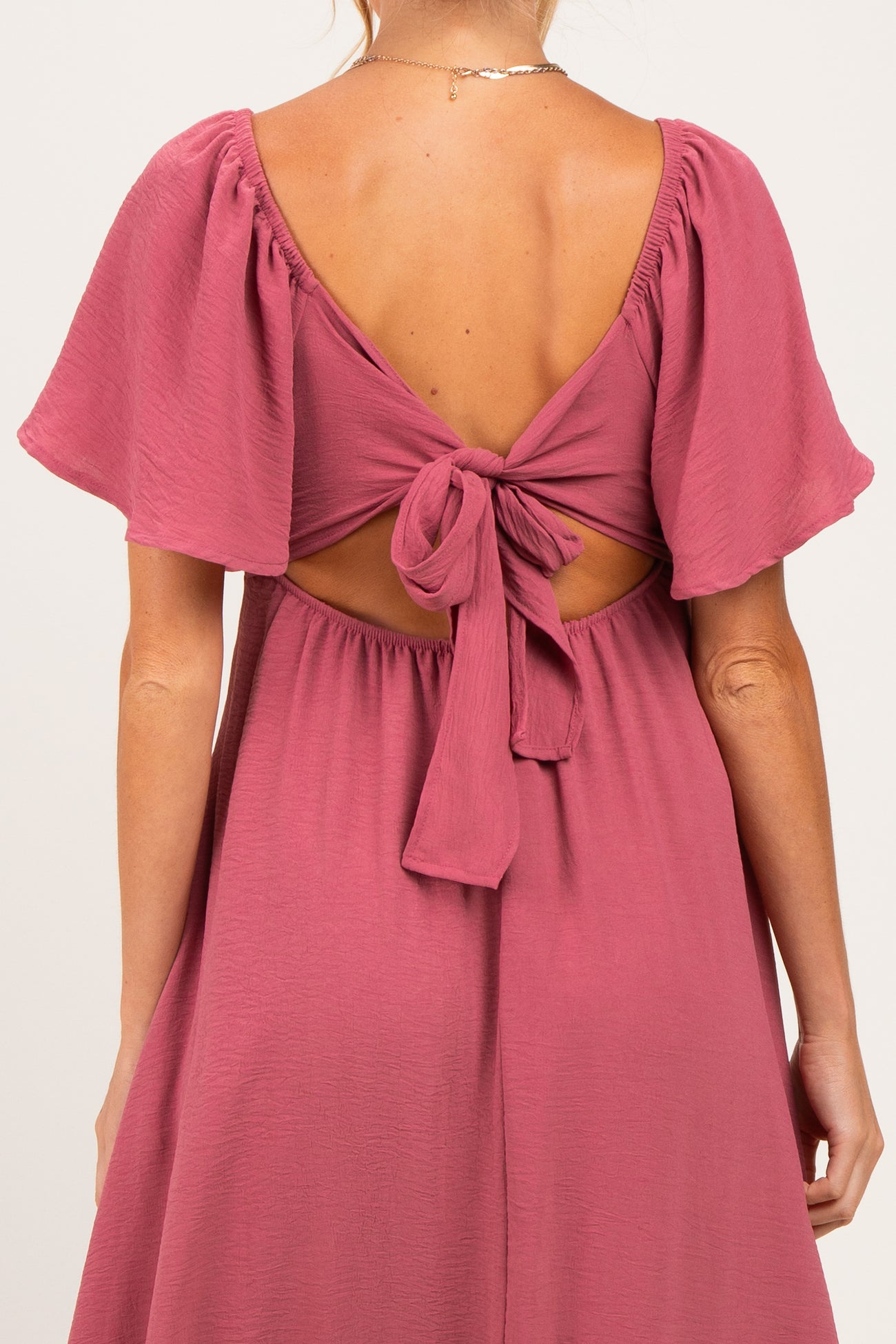 woman wearing a dusty rose maternity dress with flutter sleeves and a tie-back detail