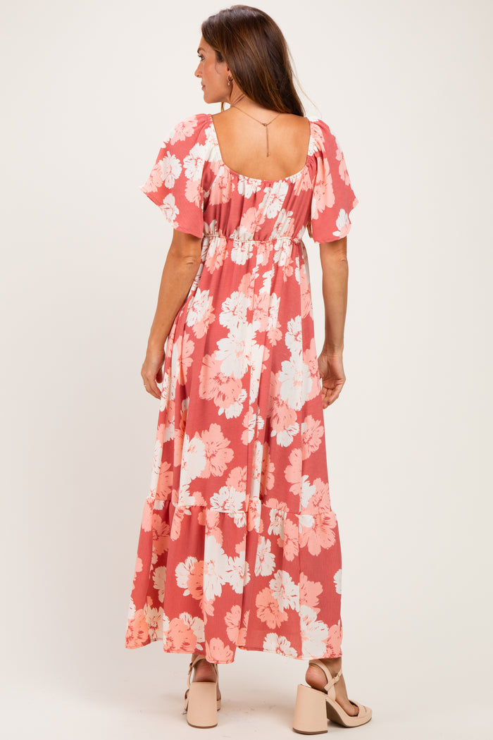 woman wearing a coral floral maxi dress with flutter sleeves and a tiered hem from the back