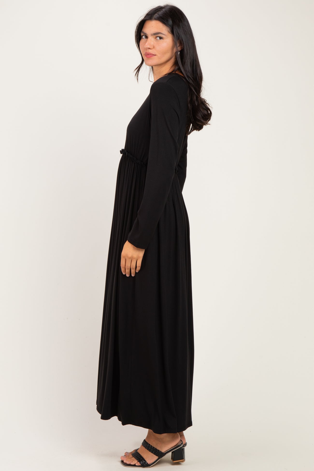 woman wearing a long black dress with long sleeves and a gathered waist detail, standing in profile
