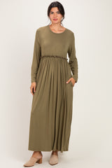 woman wearing an olive green long sleeve maxi dress with a gathered waist and pockets