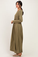 woman wearing an olive green long sleeve maxi dress with a waist tie, standing sideways against a light background