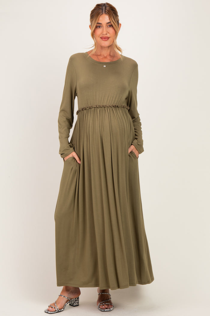woman wearing an olive green long sleeve maternity dress with a cinched waist and pockets, revealing a baby bump