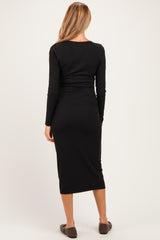 woman wearing a black ribbed maternity dress, showing a fitted silhouette and long sleeves, with the back view visible