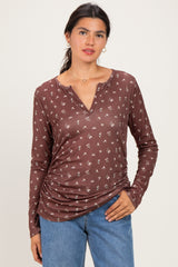 woman wearing a brown long sleeve henley top with a floral print and gathered sides, paired with light blue jeans