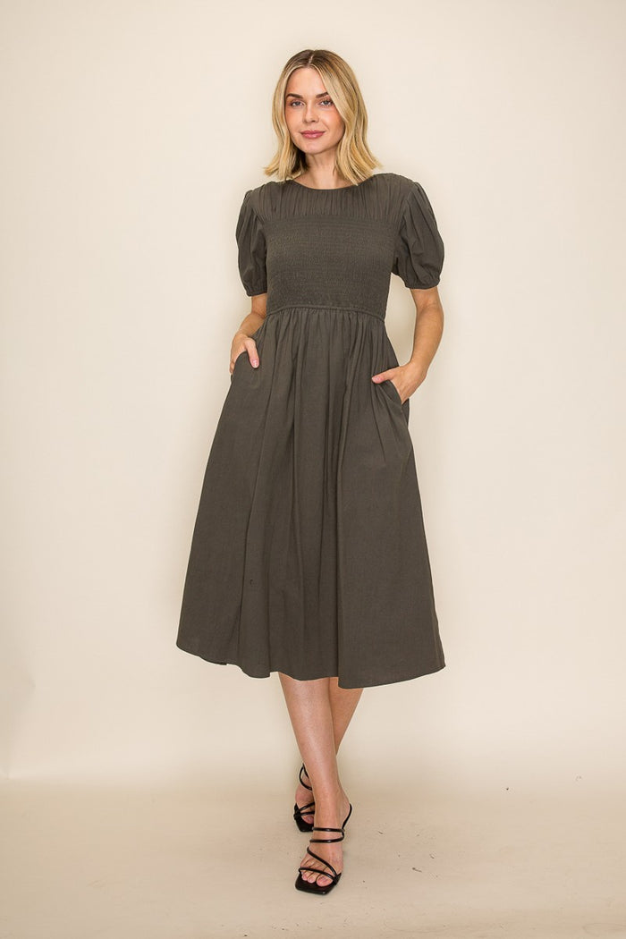 woman wearing a dark gray midi dress with puff sleeves and pockets, standing against a neutral background