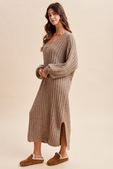 woman wearing a beige long sleeve ribbed sweater dress with side slits and styled with brown slippers