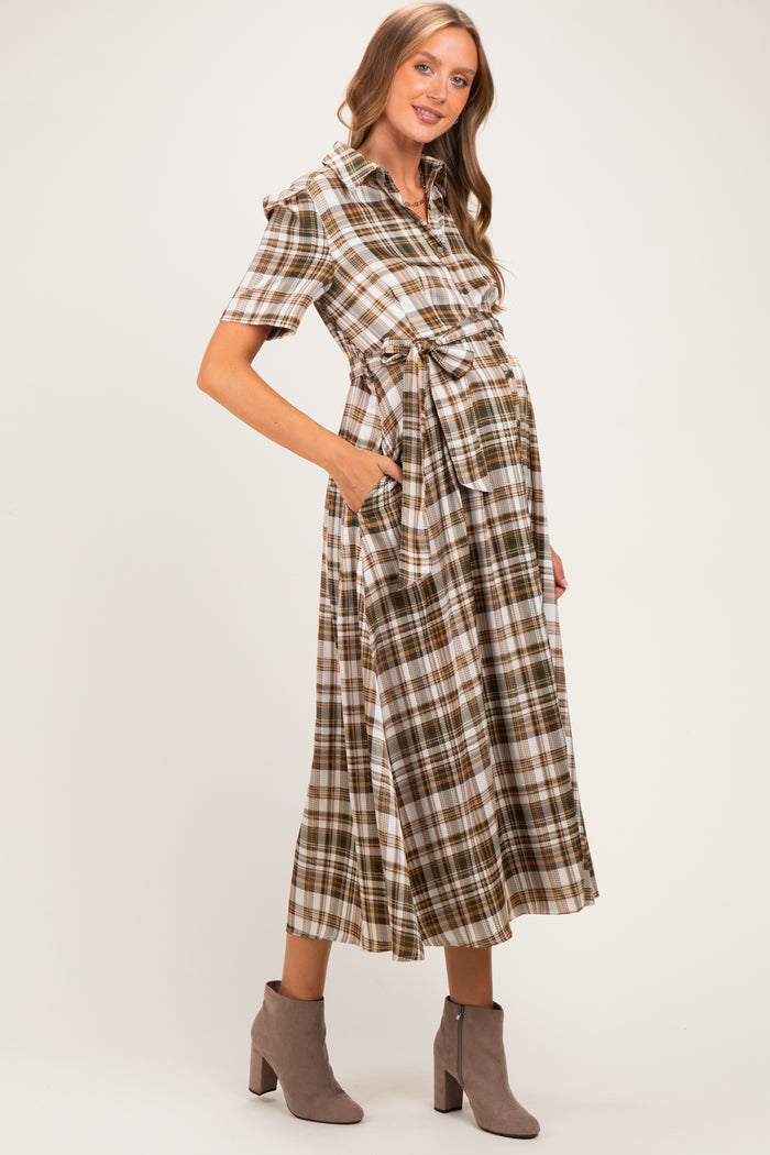woman wearing a brown and white plaid maternity dress with a tie waist and pockets, showing her baby bump