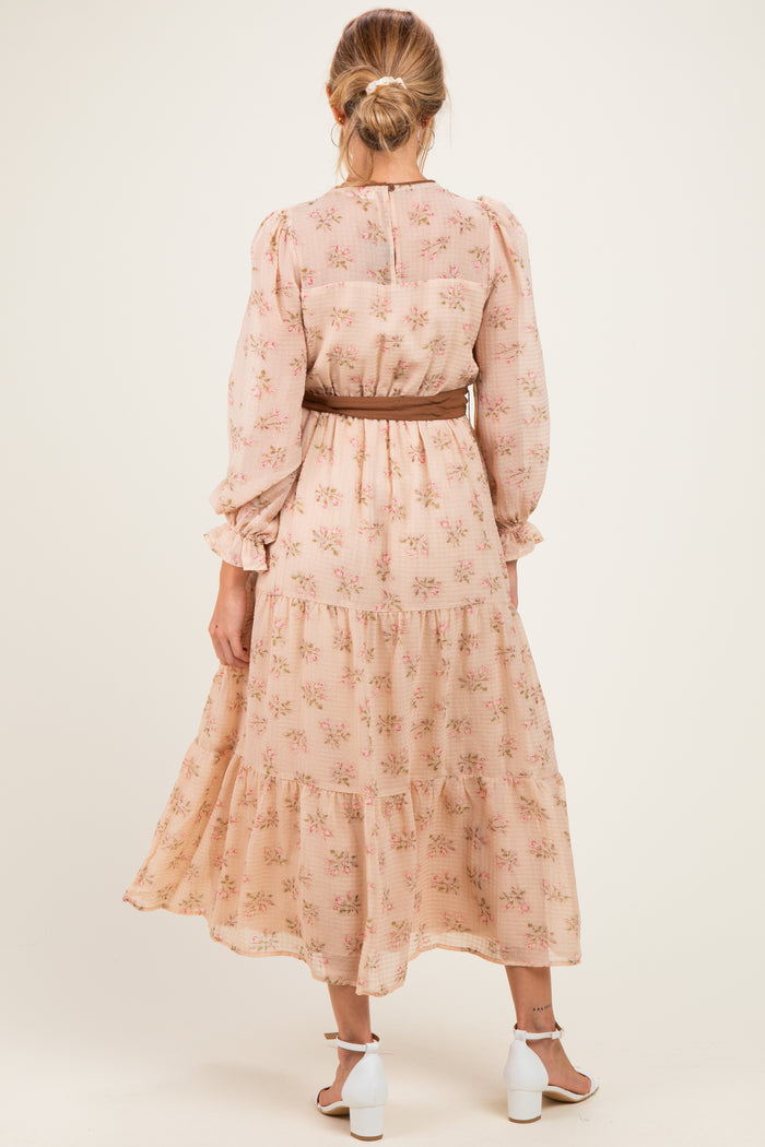 woman wearing a floral blush maternity dress with long sleeves and a tiered skirt, styled with a belt
