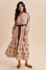 woman wearing a long sleeve beige maxi dress with floral embroidery and a tied waist belt