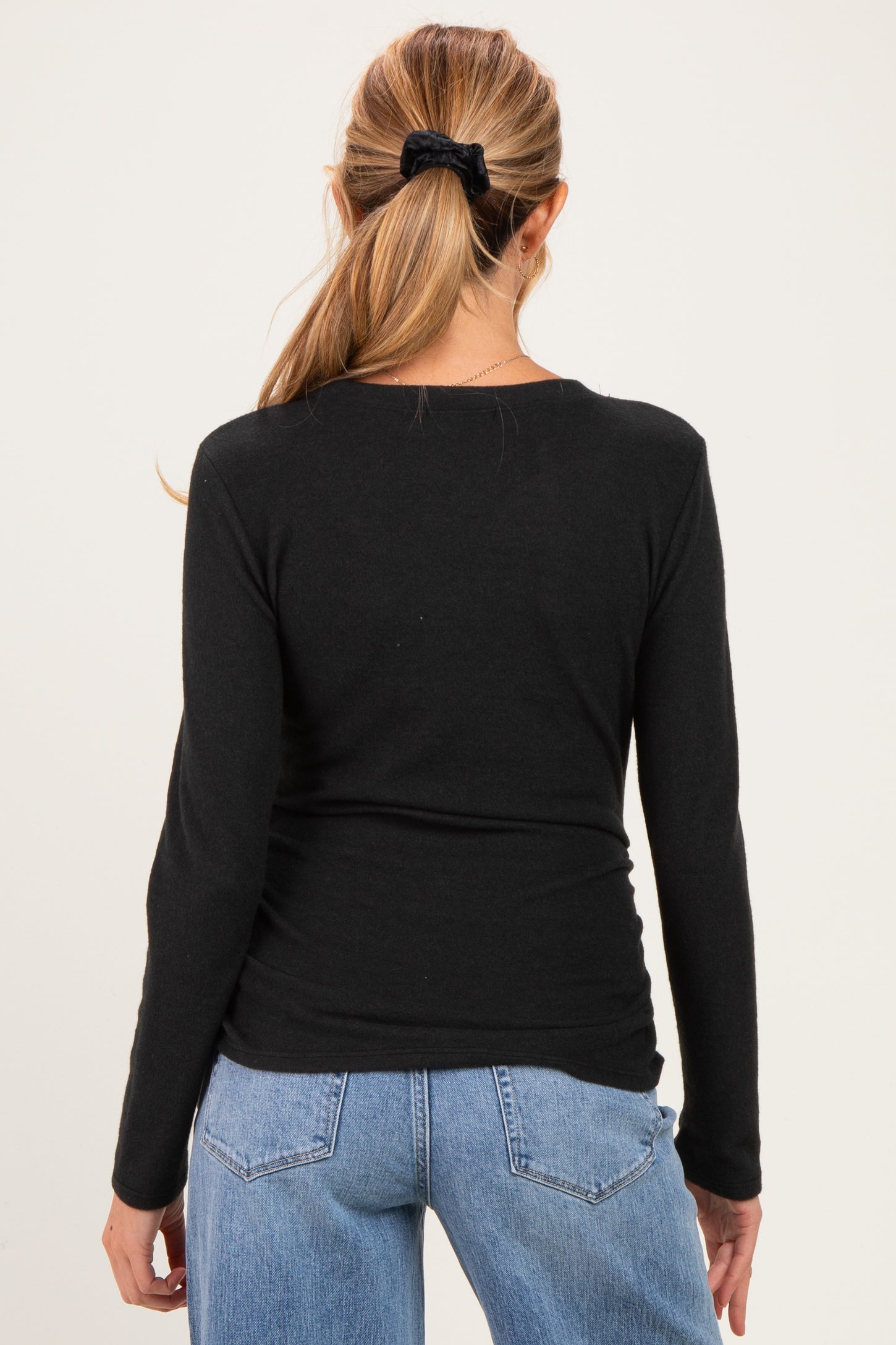 woman wearing a black long sleeve maternity top, seen from the back, paired with light blue jeans