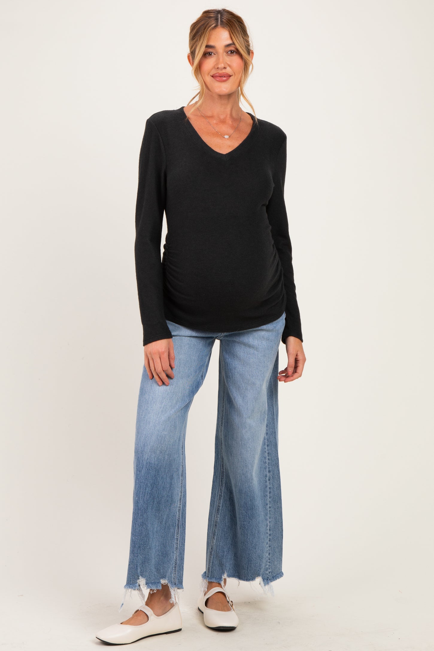 woman wearing a black v-neck maternity top and light blue wide-leg jeans, showing her baby bump