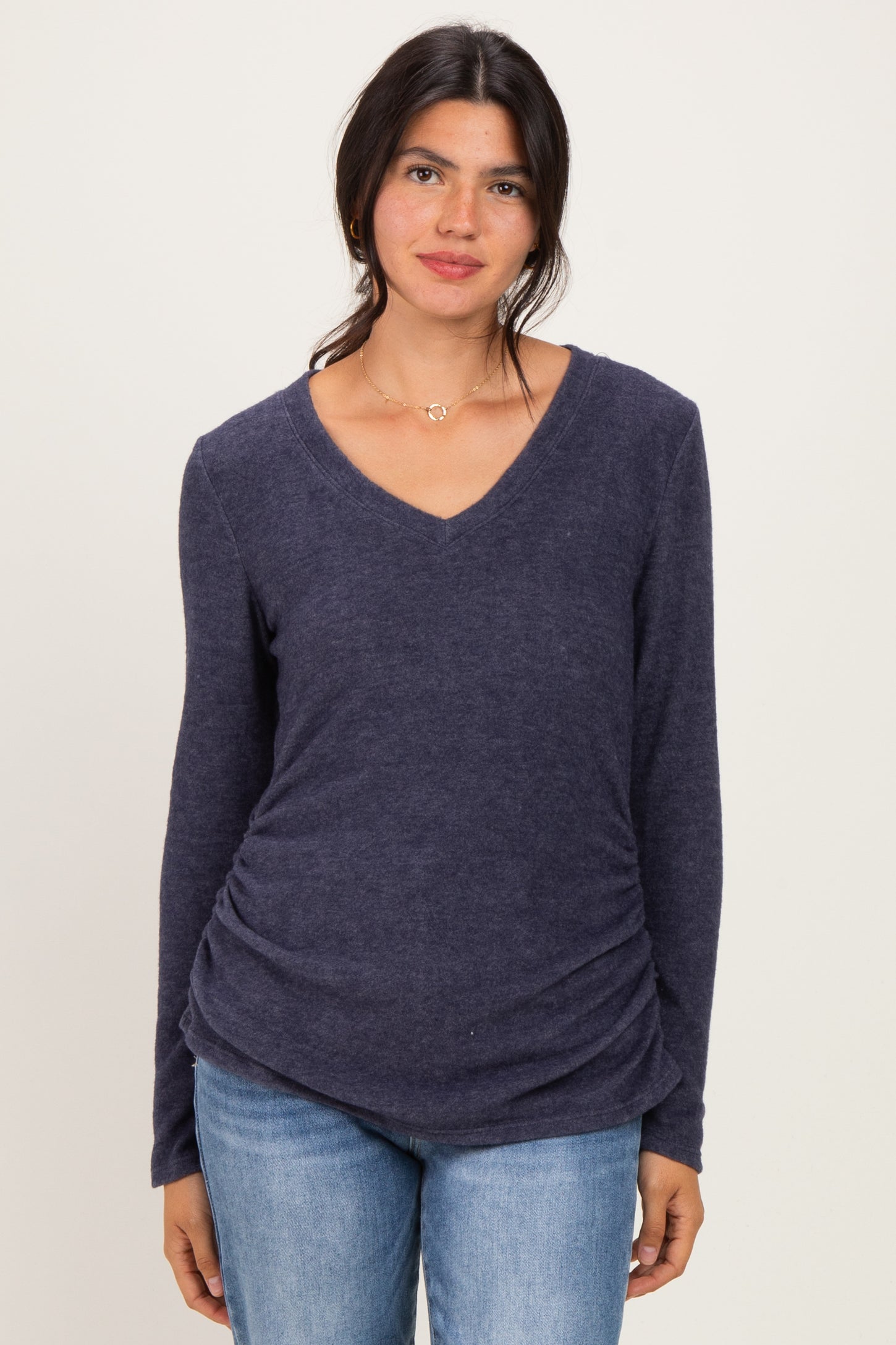 woman wearing a navy long sleeve v-neck top with ruching details and jeans