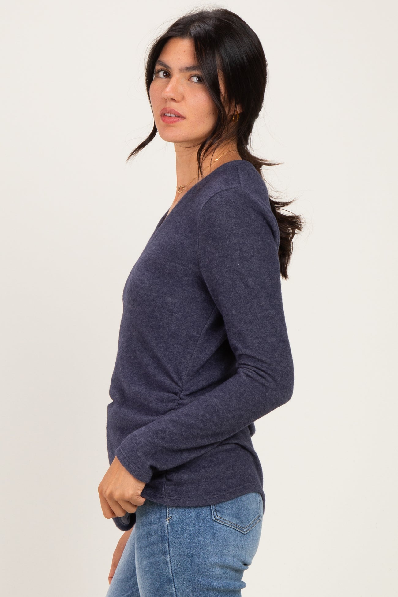 woman wearing a navy long sleeve top with a side ruching detail and blue jeans