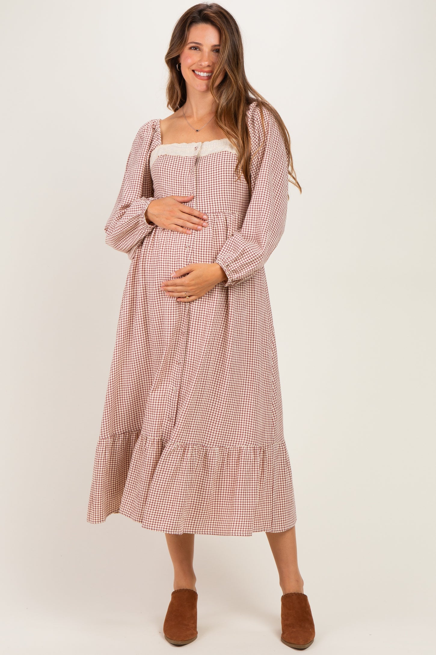 woman wearing a brown and cream checkered maternity dress with puff sleeves and a tiered skirt, holding her baby bump