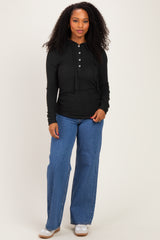woman wearing a black long sleeve henley top and blue wide leg jeans, standing with a relaxed pose