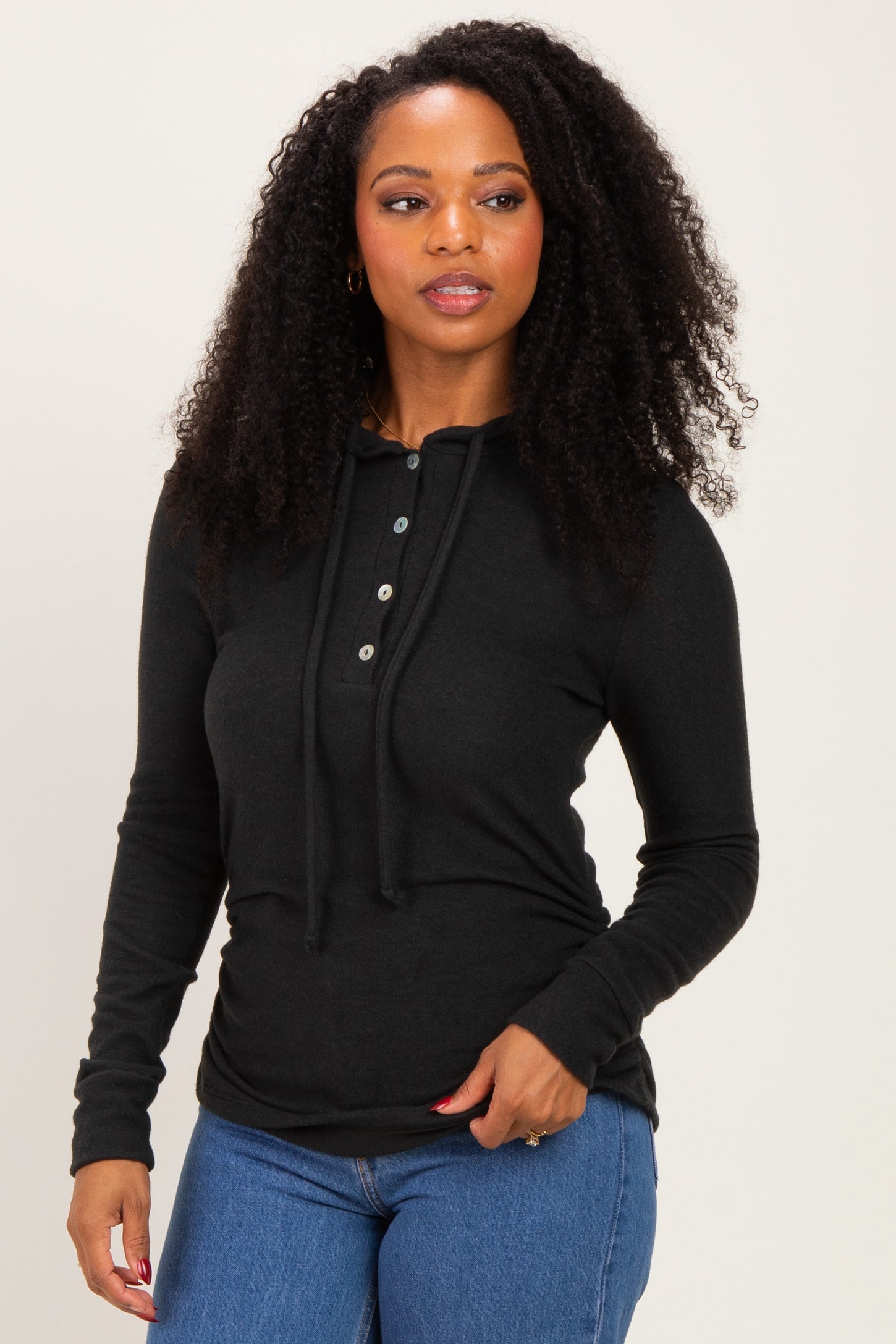 woman wearing a black long sleeve hoodie with buttons and a drawstring, paired with blue jeans