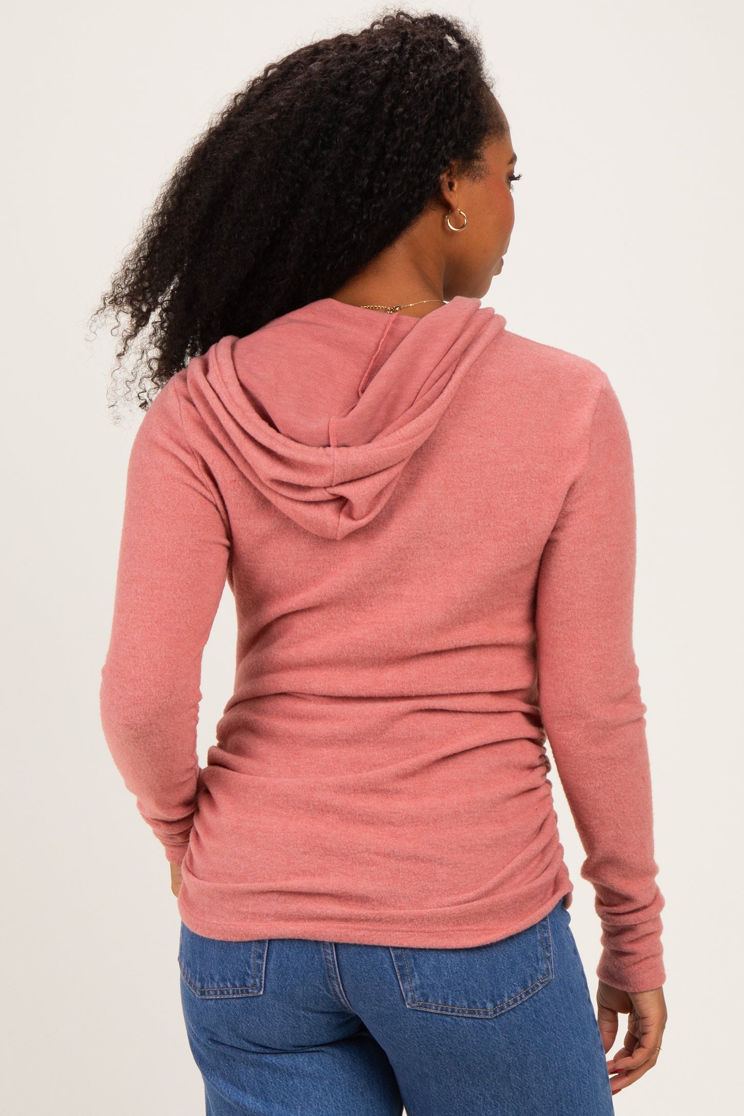 woman wearing a pink long sleeve hoodie with a hood and ruching detail on the back, styled with blue jeans
