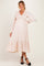 woman wearing a light pink maternity dress with a smocked bodice and long sleeves, holding her baby bump