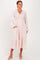 woman wearing a blush pink long sleeve dress with a smocked bodice and ruffle hem, standing with hands in pockets