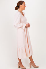 woman wearing a blush pink midi dress with a smocked bodice and flared sleeves, standing in profile with a ruffled hem