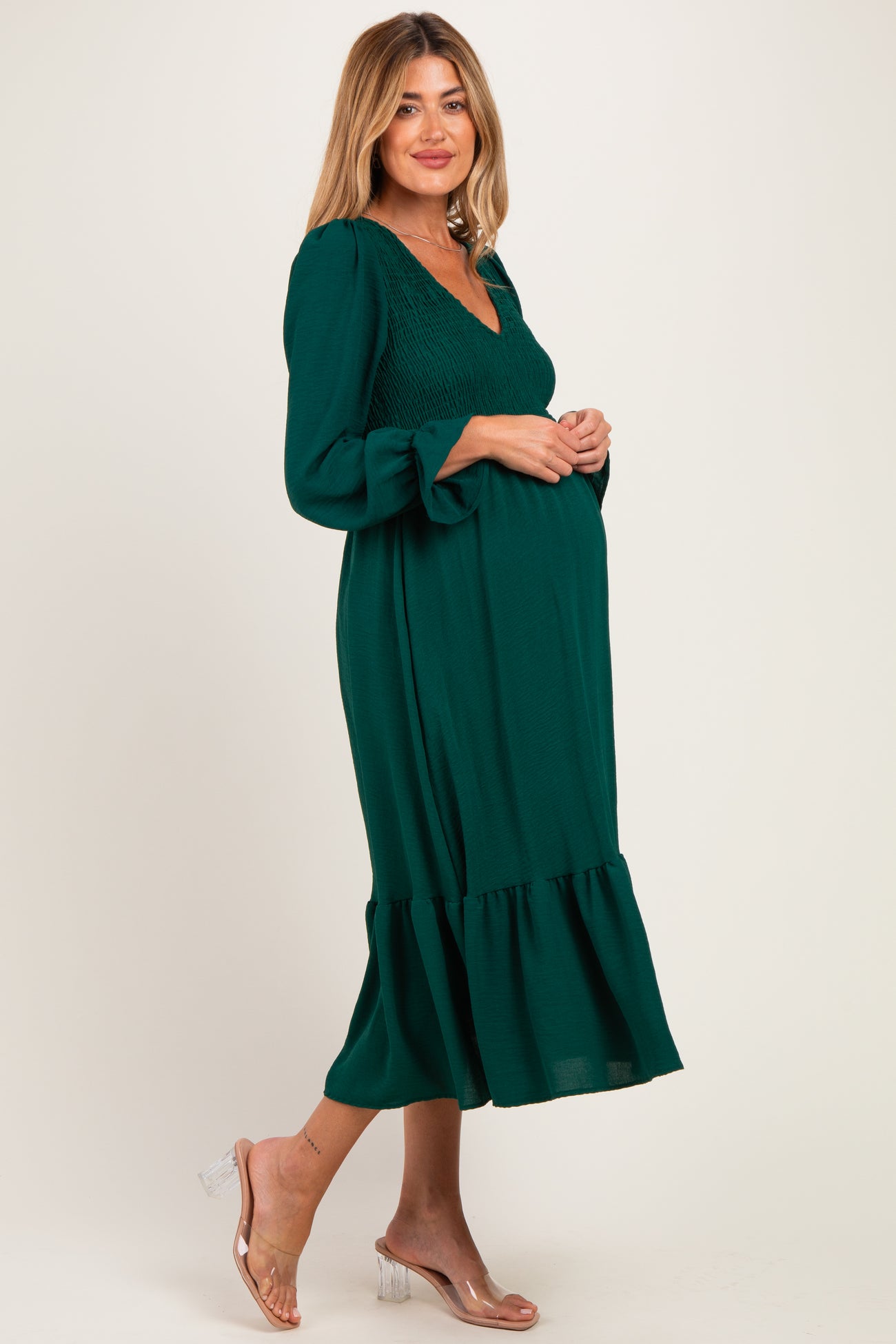 woman wearing a dark green maternity dress with smocked bodice and ruffle hem, showcasing her baby bump