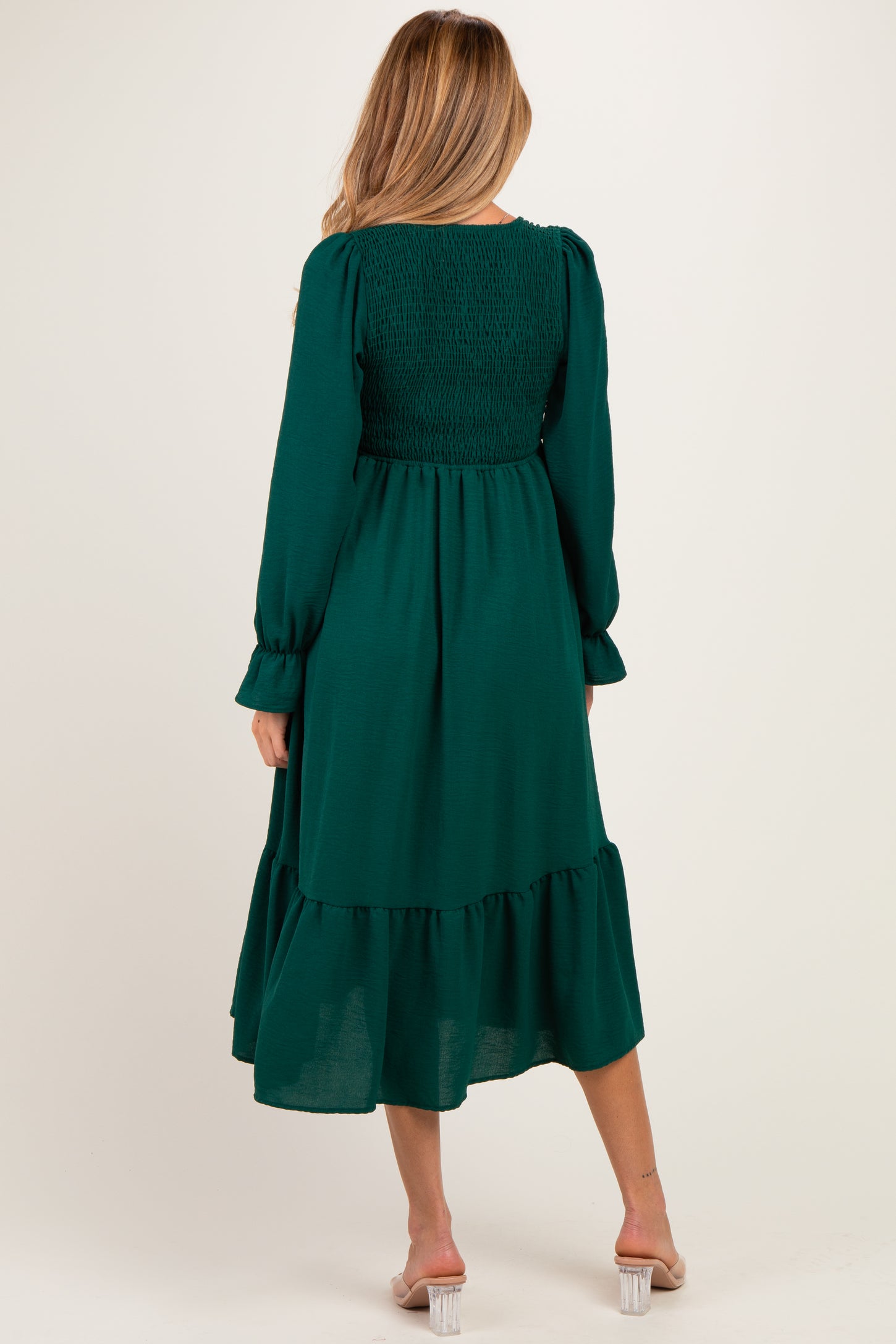 woman wearing a dark green maternity dress with smocked bodice and tiered hem, viewed from the back