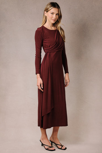 woman wearing a burgundy long sleeve wrap dress with a draped bodice and a flowy skirt