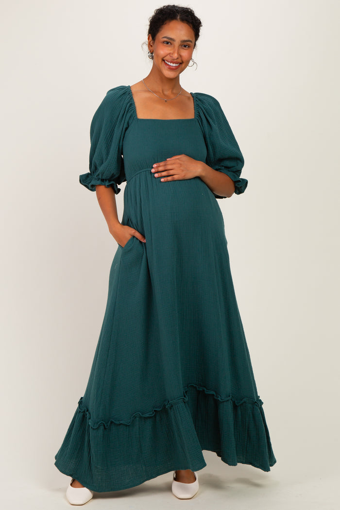 woman wearing a dark green maternity maxi dress with puff sleeves and ruffle hem, cradling her baby bump