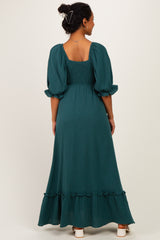 woman wearing a dark green maternity maxi dress with puff sleeves and a ruffled hemline