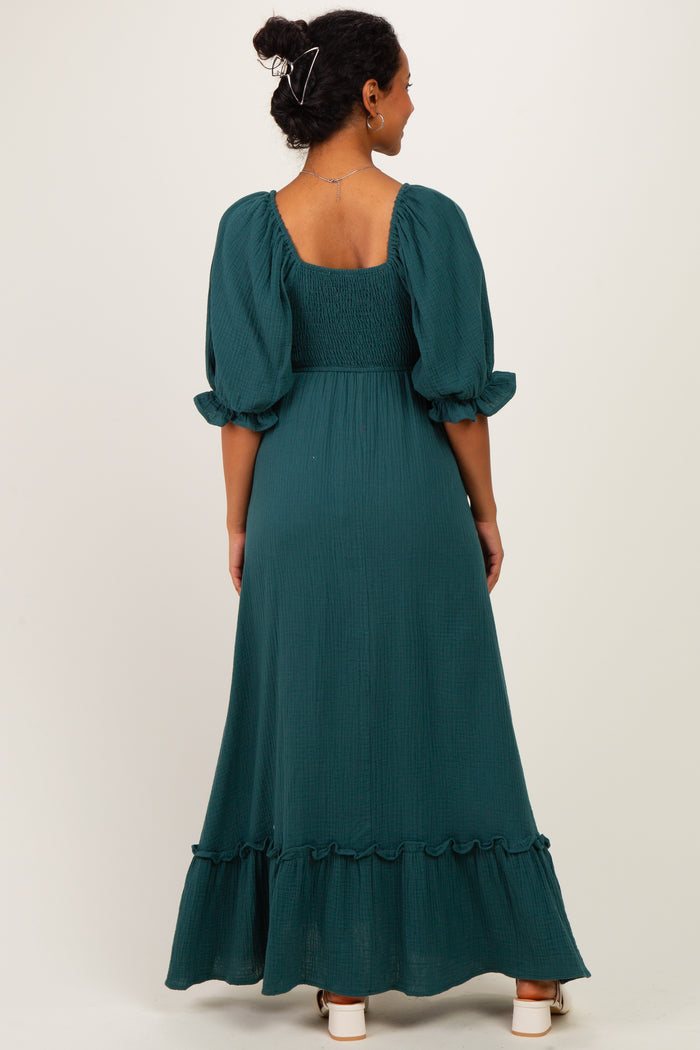 woman wearing a dark green maternity maxi dress with puff sleeves and a ruffled hemline