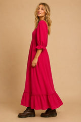 woman wearing a bright pink maxi dress with puff sleeves and ruffle hem, styled with black ankle boots