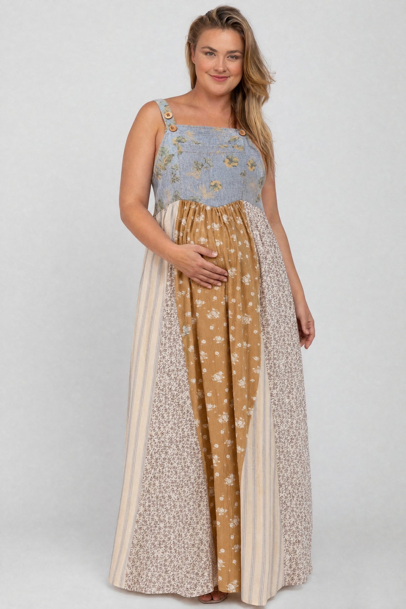 woman wearing a patchwork maternity dress with floral and striped patterns, cradling her baby bump