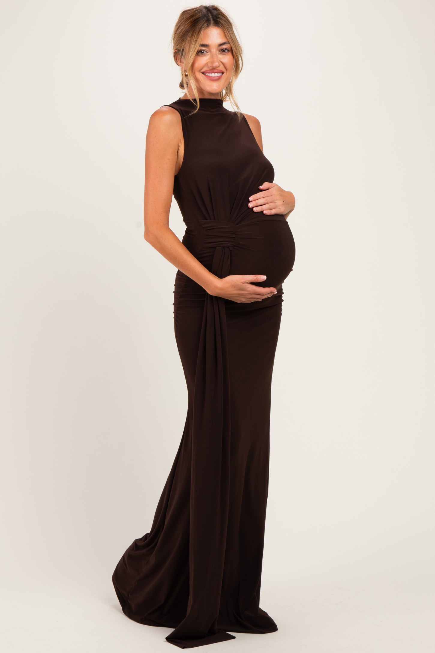 woman wearing a dark brown sleeveless maternity gown, posing and holding her baby bump