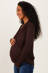 woman wearing a brown maternity wrap top and showing her baby bump while smiling