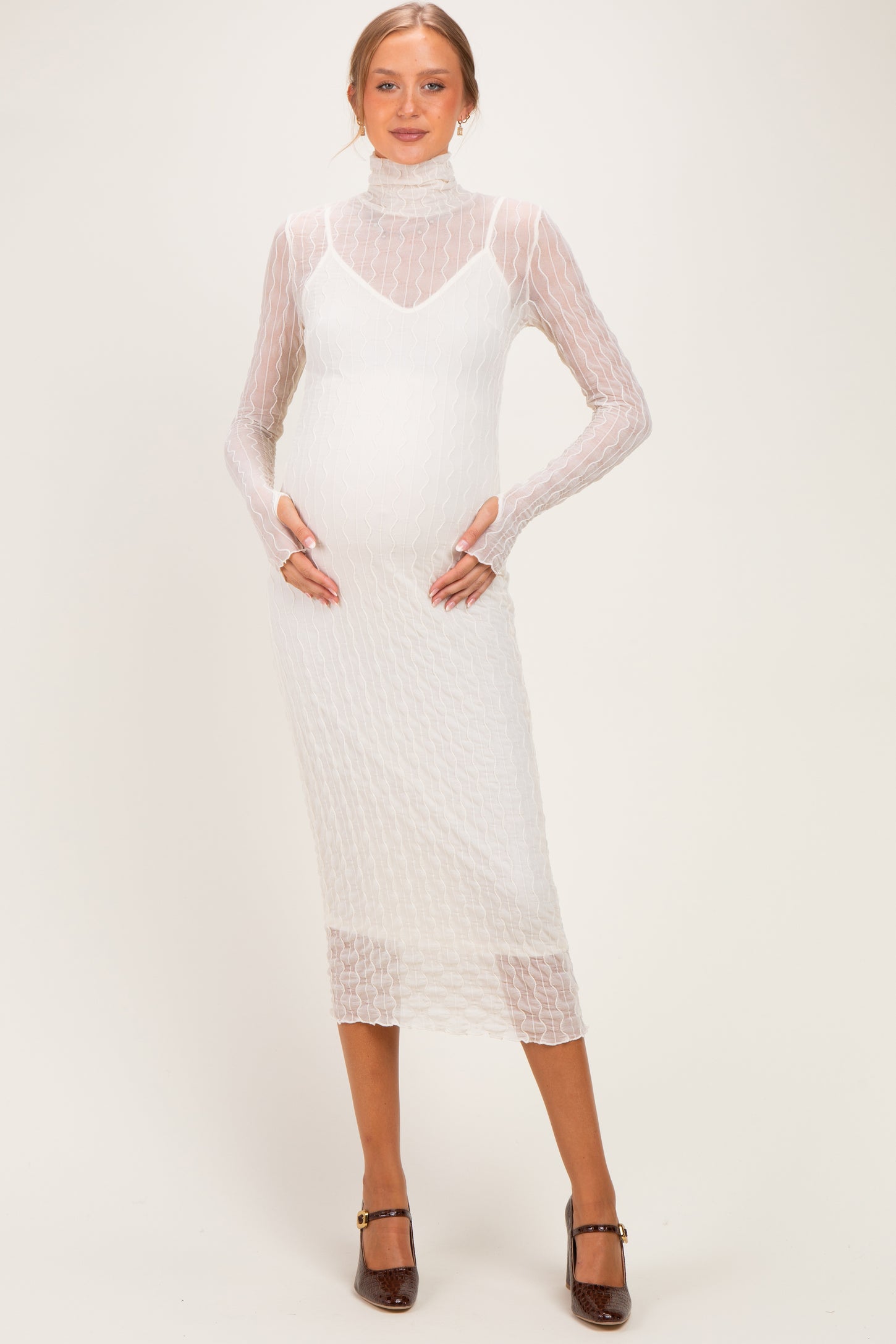 woman wearing a white fitted maternity dress with a textured pattern and long sleeves, showing her baby bump
