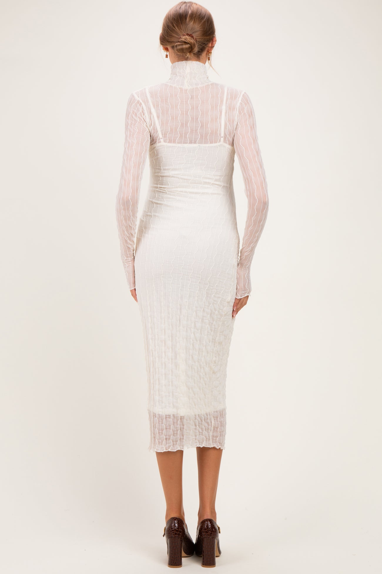 woman wearing a white maternity dress with long sleeves and a fitted silhouette, showing a baby bump from the back