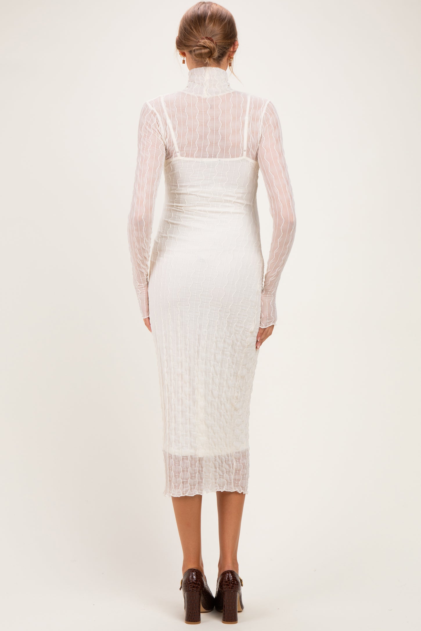 woman wearing a white maternity dress with long sleeves and a fitted silhouette, showing a baby bump from the back